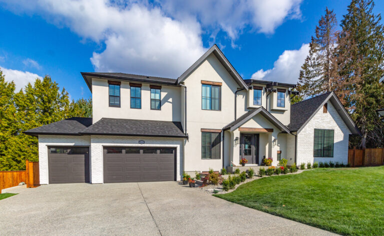Wide angle shot of front view of luxury two garage big white home with luscious green grass  on a blue sky day in the suburbs
